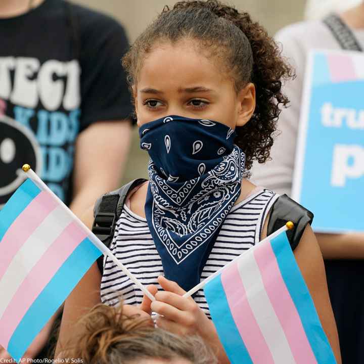 A black child holding two transgender flags
